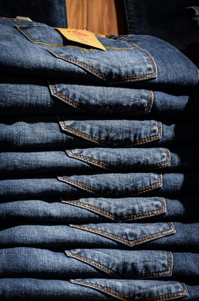 jeans pants blue shop 52518 52518 Neatly stacked blue jeans with visible price tag in retail setting.